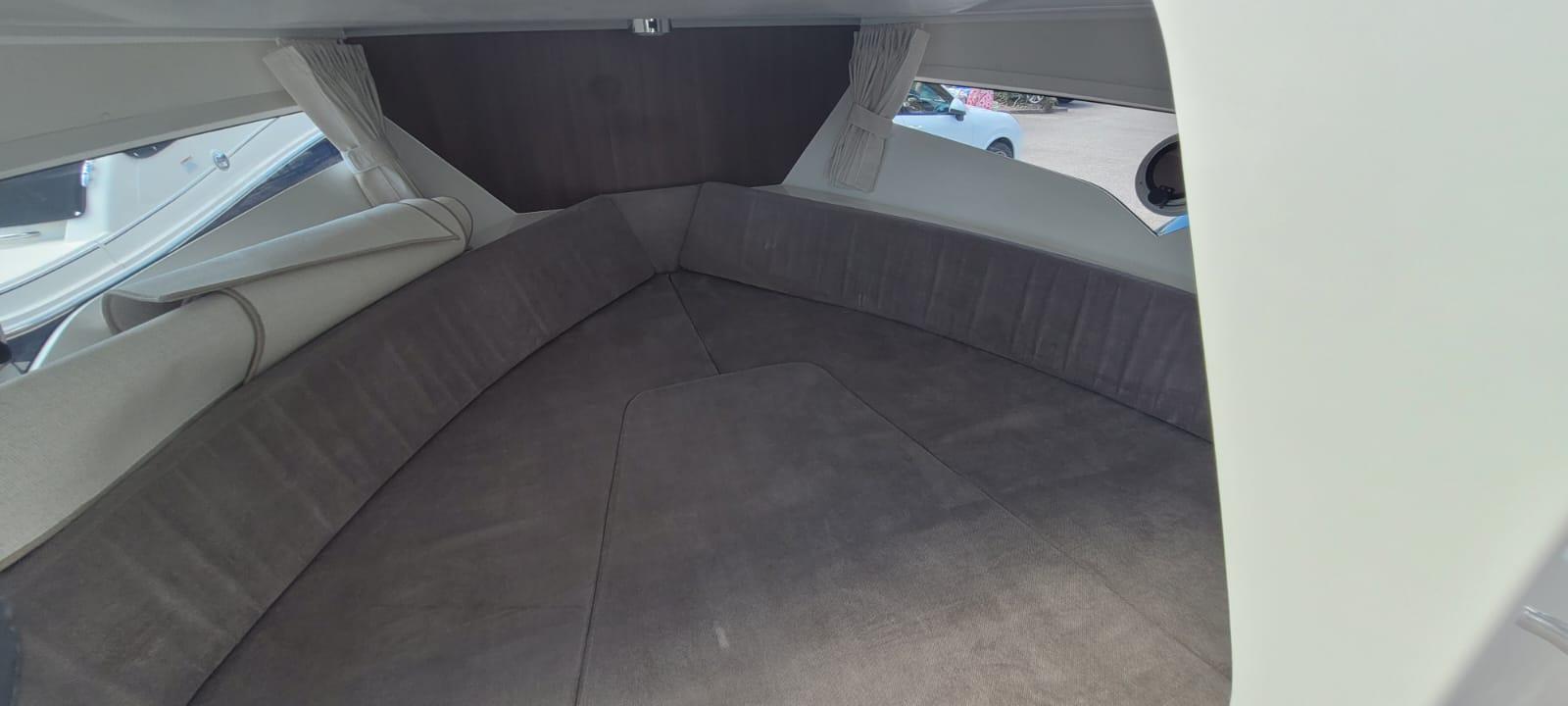 Cozy boat interior with curved seating and soft gray upholstery, featuring large windows and light curtains.